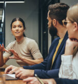 Young businesswoman leading a discussion during a meeting with her colleagues. Group of diverse businesspeople working together in a modern workplace. Business colleagues collaborating on a project.