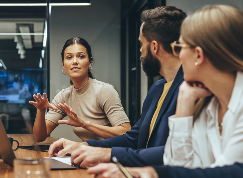 Young businesswoman leading a discussion during a meeting with her colleagues. Group of diverse businesspeople working together in a modern workplace. Business colleagues collaborating on a project.